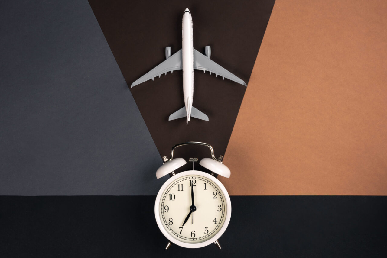 White alarm clock and airplane model on a paper background, top view